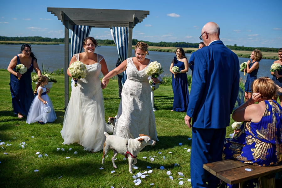 A newly married lesbian couple walk down the isle with their dog.